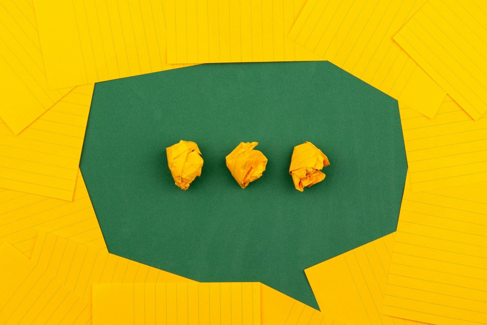 Trois papiers jaunes froissés sur une surface verte entourés de papiers lignés jaunes.